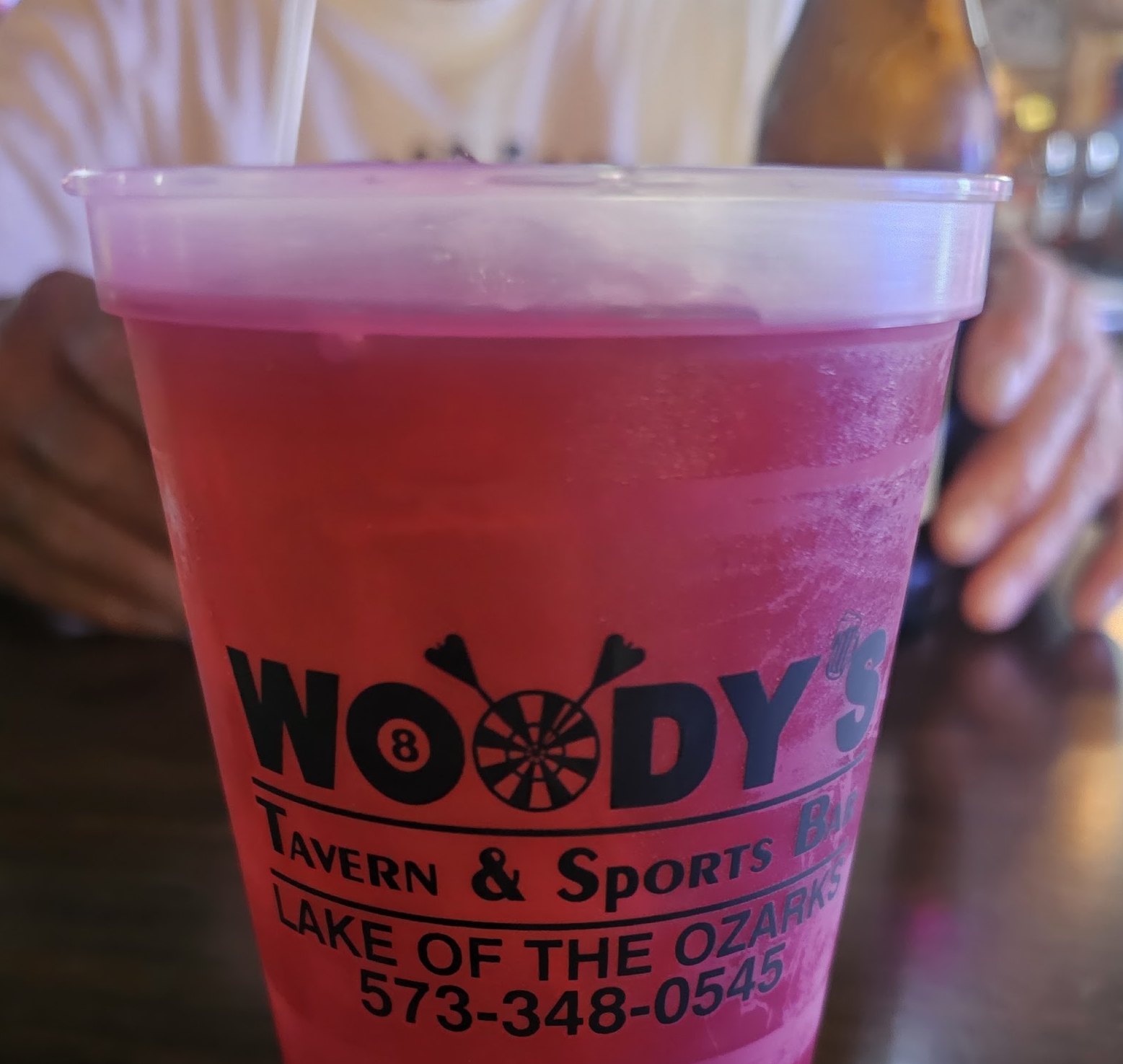 A Woody's cup printed with the eight ball and dartboard wordmark and the phone number